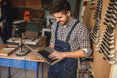 Young carpenter working on a laptop in his workshop. Schlagwort(e): workshop, carpentry, occupation, carpenter, laptop, professional, craftsman, handyman, industry, craft, job, timber, lumber, woodwork, handmade, tools, old, business, manual, worker, plan, expertise, computer, pursuit, art, person, careers, equipment, activity, craftsmanship, talent, decoration, lifestyle, wooden, classic, handicraft, design, skill, capability, career, style, networking, working, woodworker, online, using, smiling, workman, indoors, workshop, carpentry, occupation, carpenter, laptop, professional, craftsman, handyman, industry, craft, job, timber, lumber, woodwork, handmade, tools, old, business, manual, worker, plan, expertise, computer, pursuit, art, person, careers, equipment, activity, craftsmanship, talent, decoration, lifestyle, wooden, classic, handicraft, design, skill, capability, career, style, networking, working, woodworker, online, using, smiling, workman, indoors