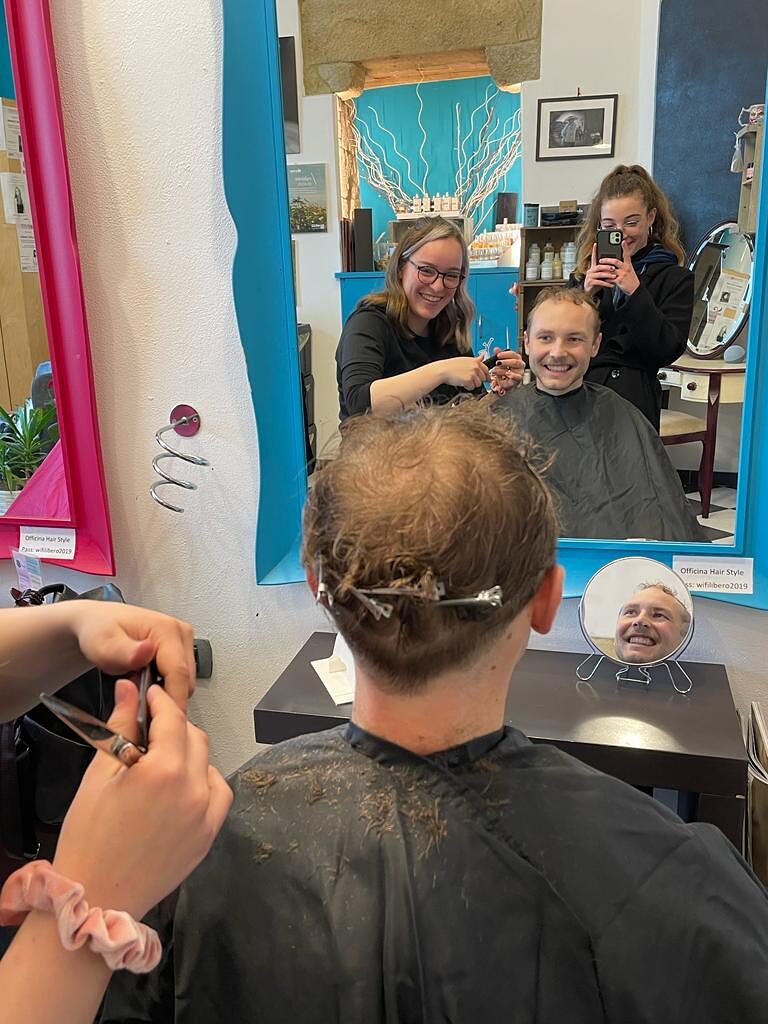 Vier Gewerke in einem Bild: Während Friseurin Dana dem Betonbauer Max-Luca die Haare schneidet, dokumentiert die Malerin und Lackiererin Celina das Ganze in ihrer Zusatzfunktion als Vor-Ort-Fotografin.