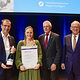 Sandra Mayer, Bestmeisterin im Schilder- und Lichtreklamehersteller-Handwerk, erhält von Vizepräsident Alexander Kotz (1.v.l.), Vizepräsident Peter Kudielka (2.v.r.) und Präsident Rainer Reichhold (1.v.r.) ihre Schmuckurkunde und eine Sektflasche. 